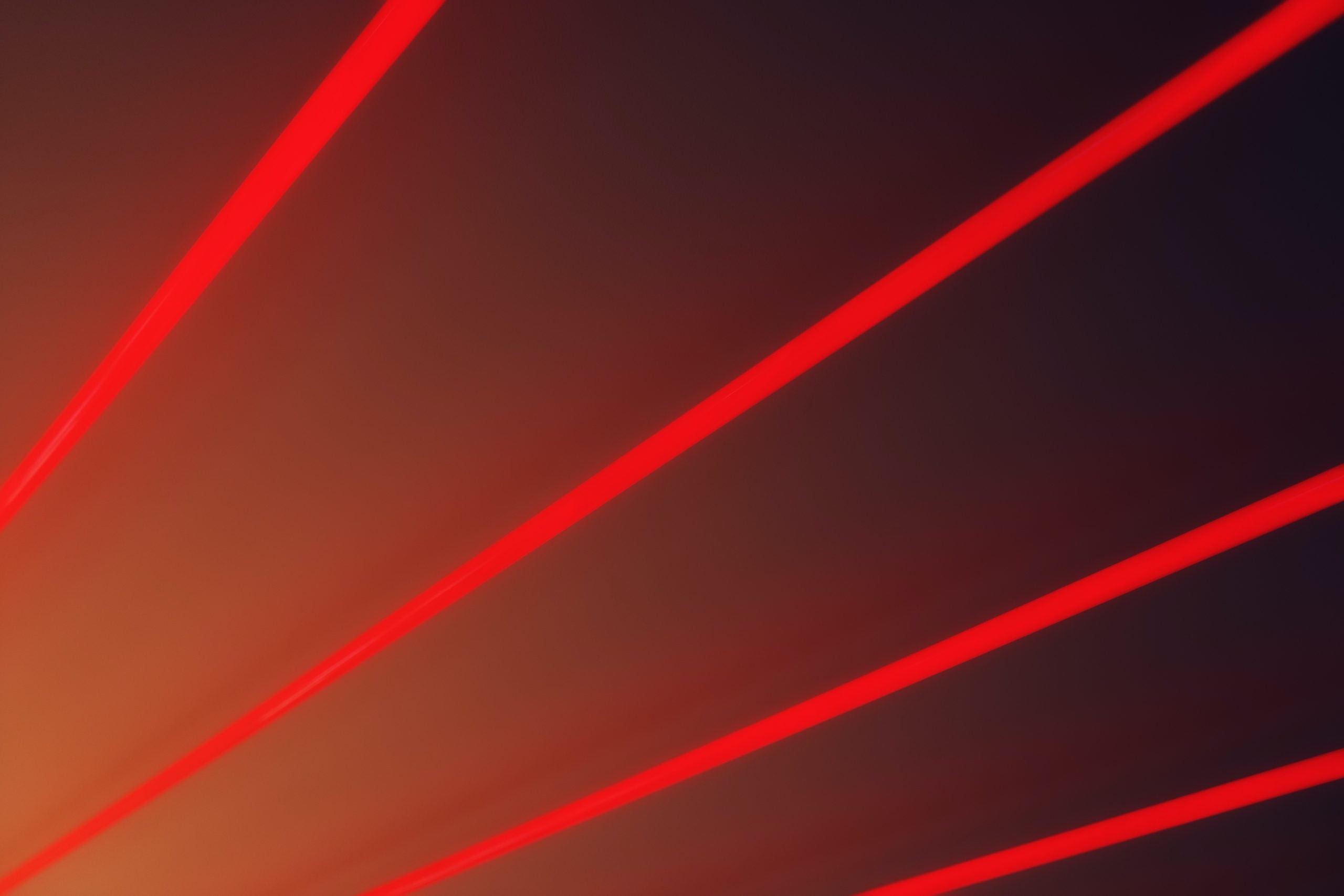 A picture showing four red straight, laser-like lines representing the sensors that make up OT and IoT devices. This article is about the top IoT security solutions which.look the next generation of smart devices and systems powering consumer and organization locations.