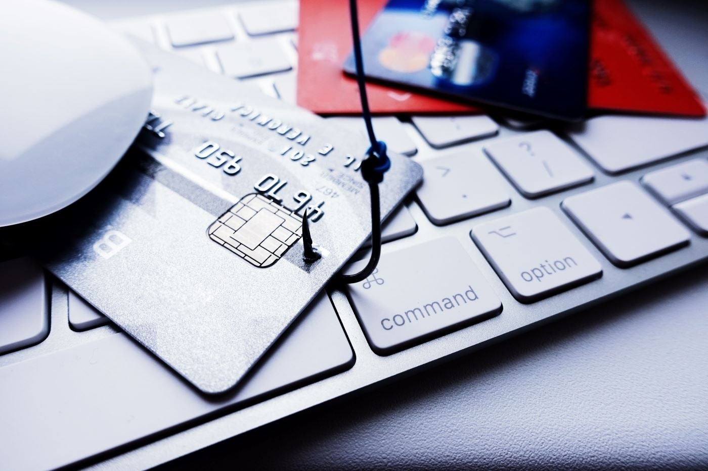 A fishing hook stuck to a credit card over a keyboard signaling phishing.